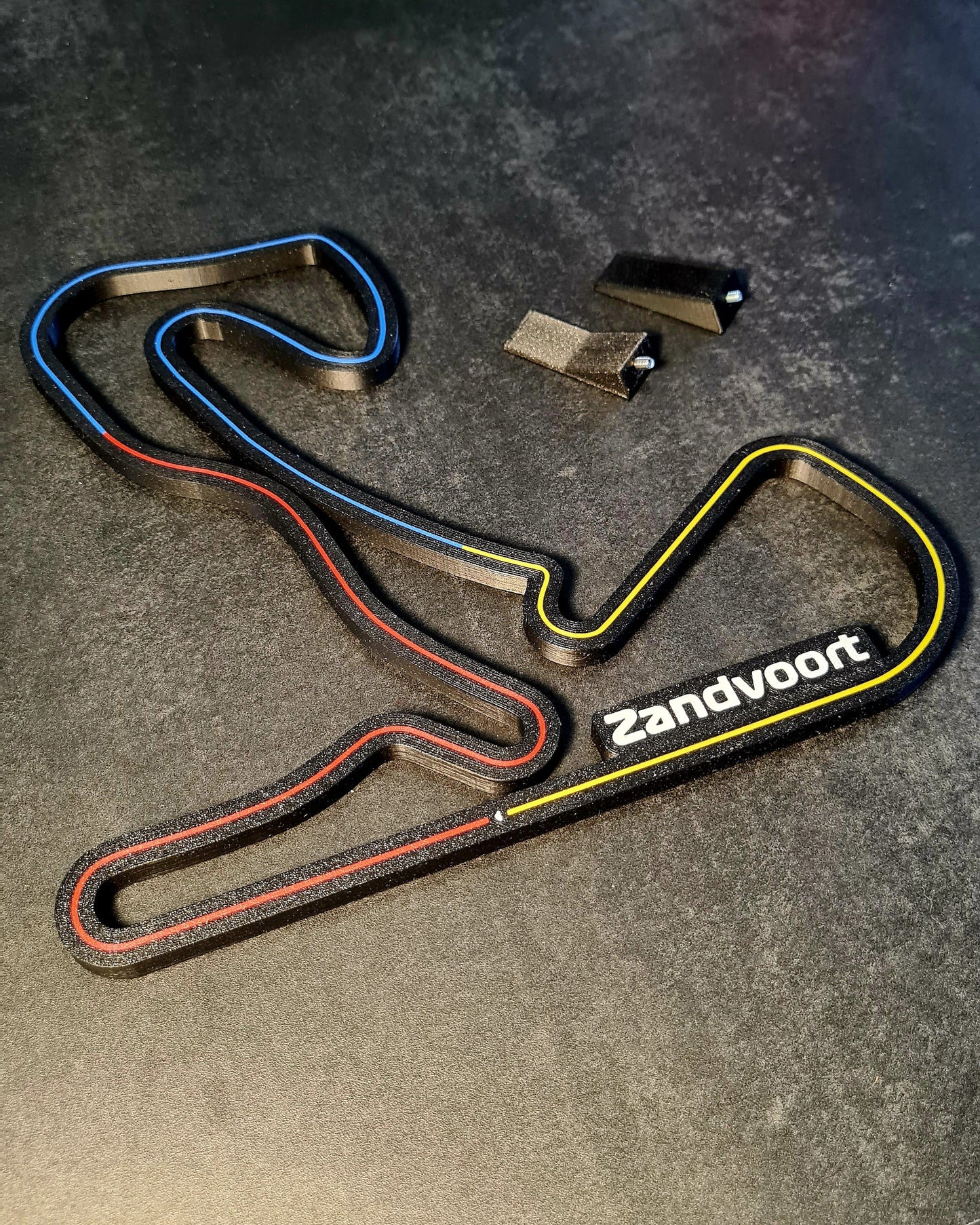 Track layout display labeled "Zandvoort" in a stylized design ideal for Formula 1 and sim racing fans, featuring color-coded sectors on a dark surface with accompanying miniature magnetic stands.