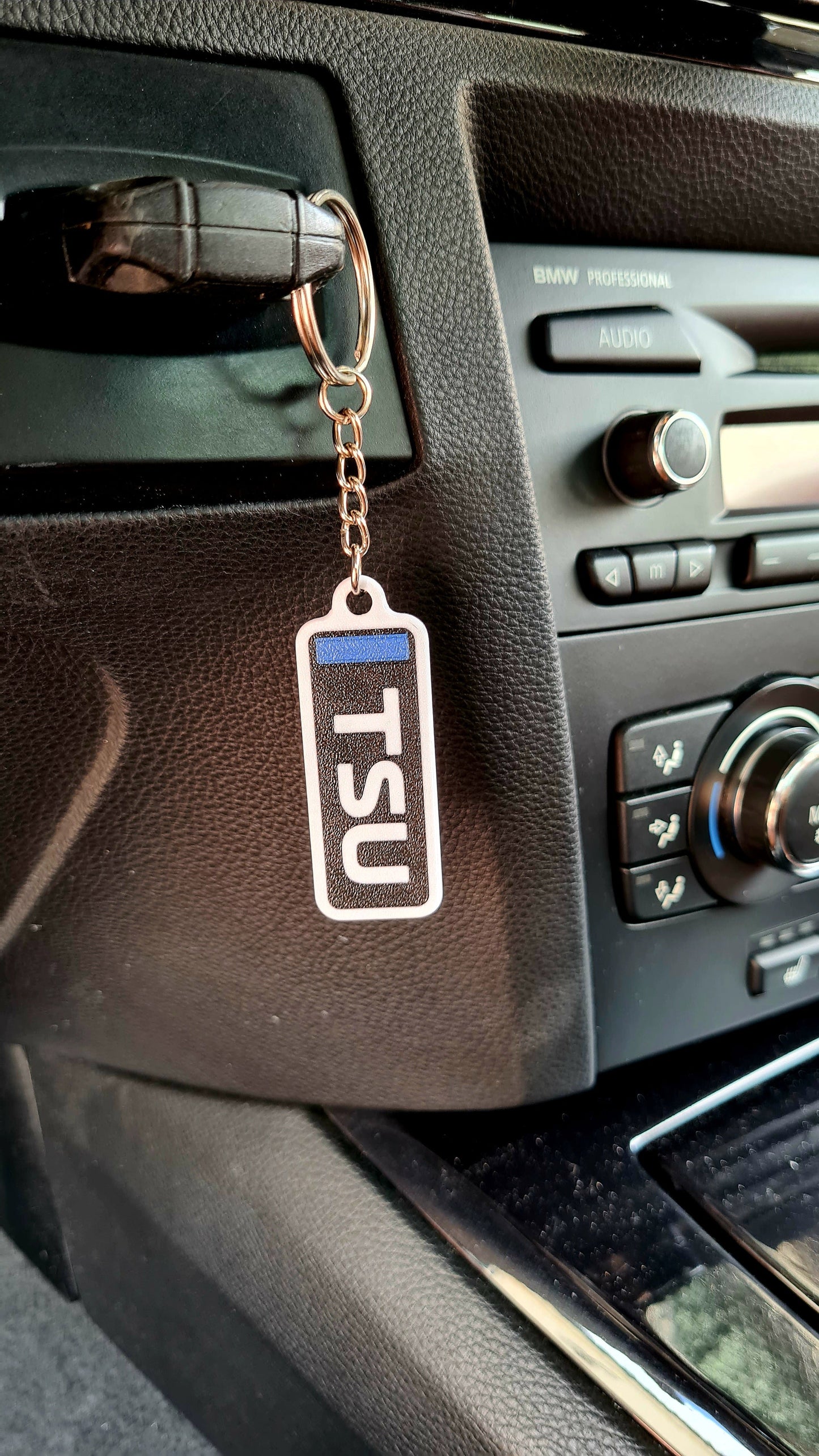 Custom McLaren keychain featuring Norris-Piastri design, hanging in a car. It displays a "VER" text in black with a blue stripe, highlighting the theme typical of F1 racing team aesthetics.