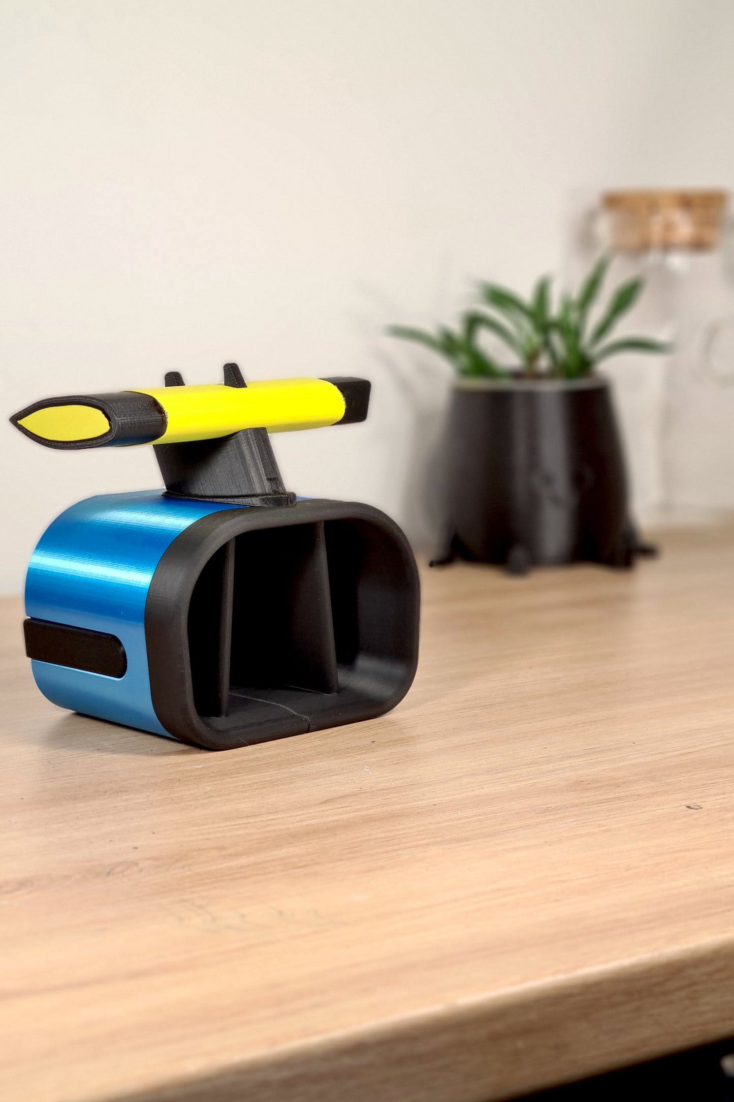 Customized Alpine F1 racing airbox replica on a desk, featuring blue and yellow colors, with a rear-view resembling a race car spoiler. Background includes a potted plant, enhancing its appeal as a collector's item for racing fans.