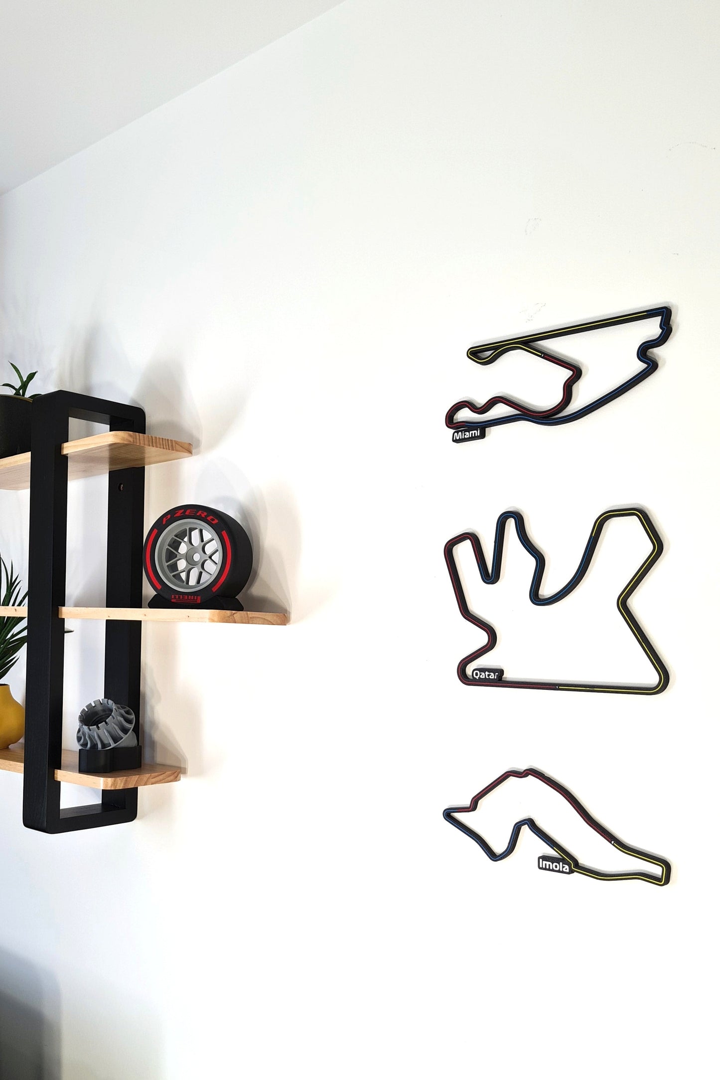 Wall-mounted shelf displaying decorative items including three racing circuit track outlines labeled Miami, Qatar, and Imola, alongside model car tires, on a minimalistic white background.