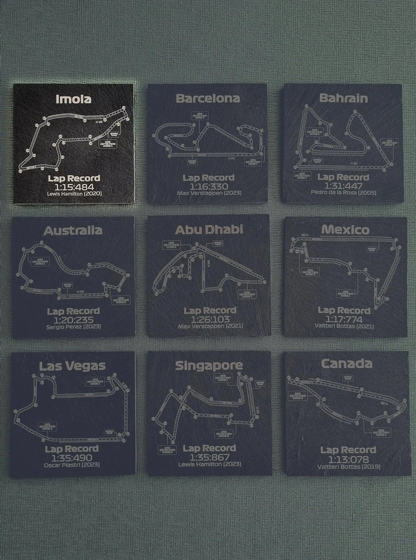 Nine dark slate F1 circuit map coasters displaying track layouts, lap records, and driver names, ideal F1 fan gift.