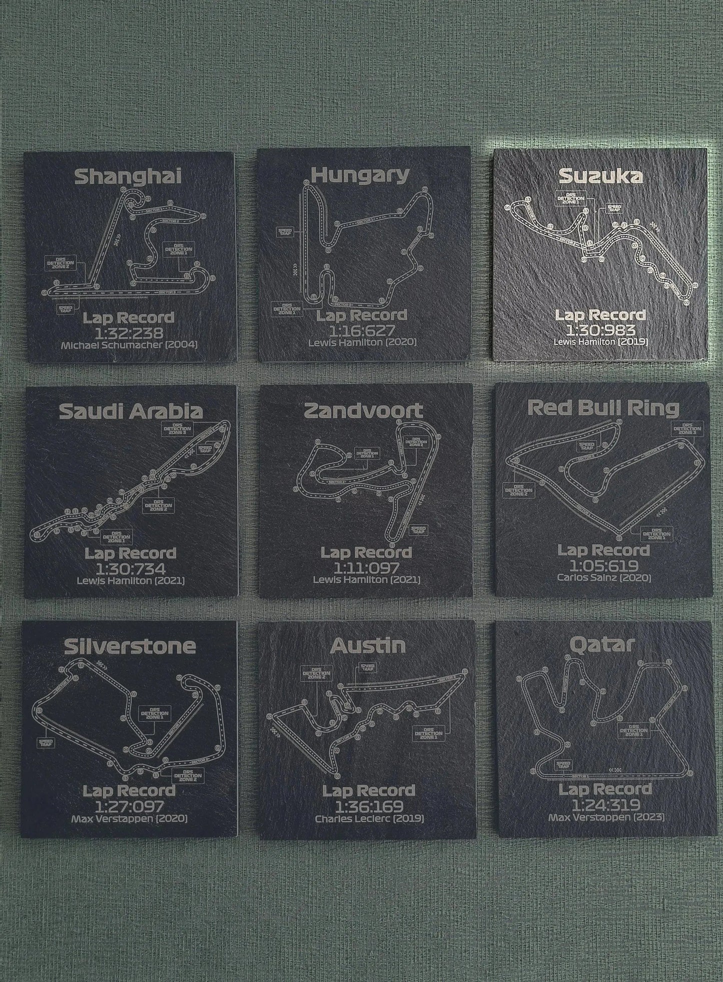 Set of nine dark grey slate F1 track coasters featuring various Grand Prix circuits and lap records, perfect unique F1 fan gift.
