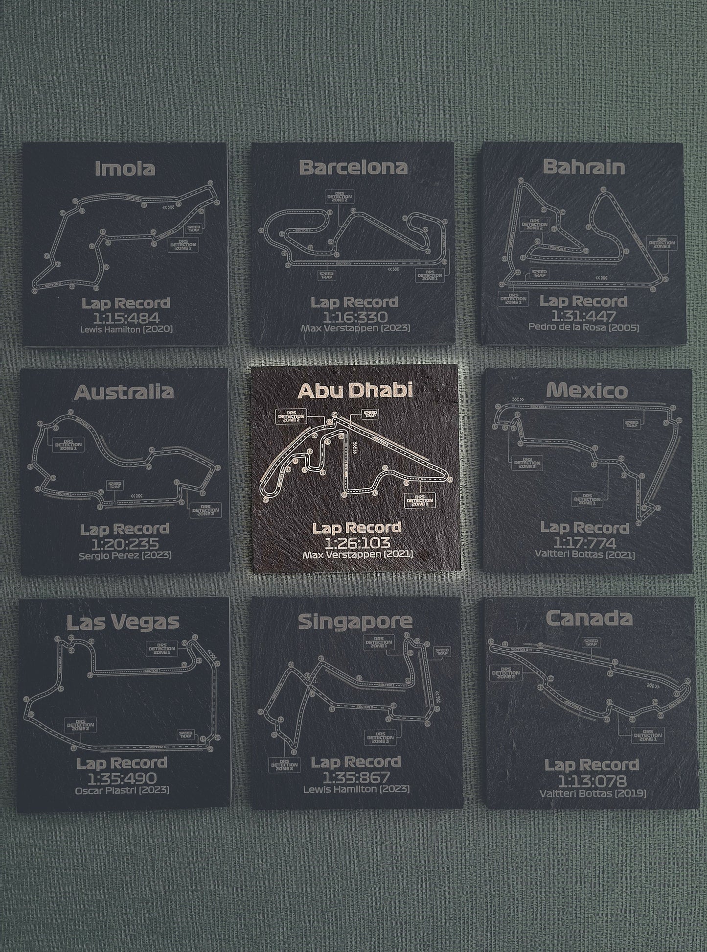 Set of nine dark glass coasters, each featuring different Formula 1 track outlines such as Abu Dhabi, Barcelona, and Mexico, with recorded fastest lap times and drivers' names like Max Verstappen and Lewis Hamilton.