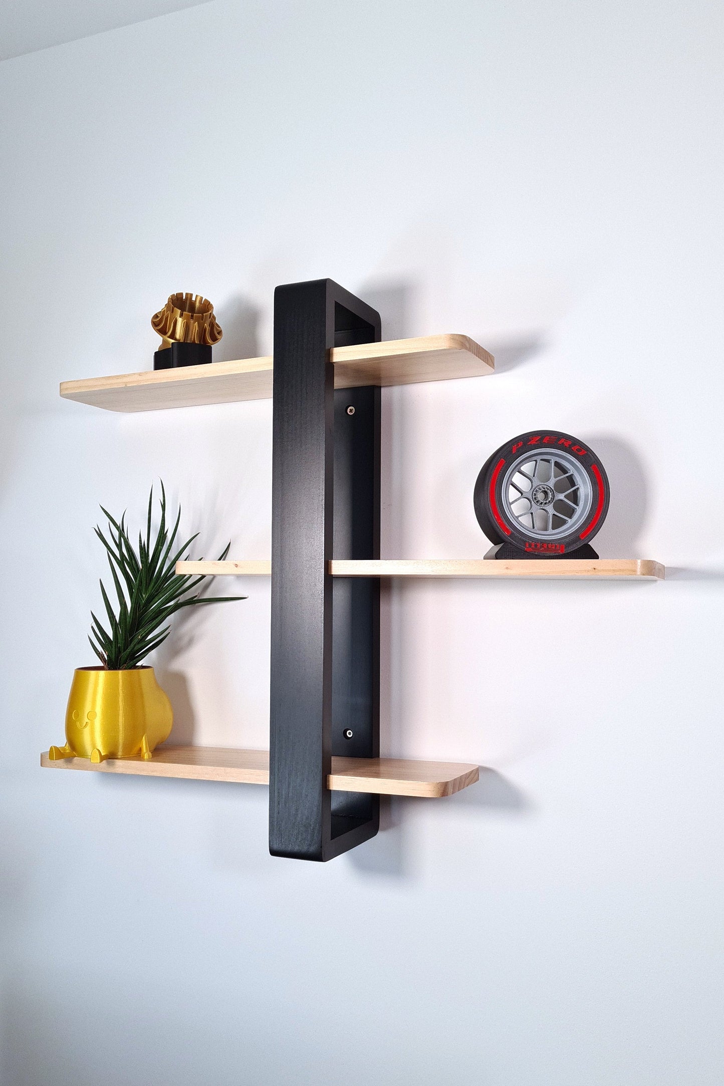 A replica of a Formula 1 tire and rim, labeled "P ZERO", displayed on a black stand. The rim is silver with a detailed design, combined with a black tire featuring red accents, placed on a wooden shelf against a white background.