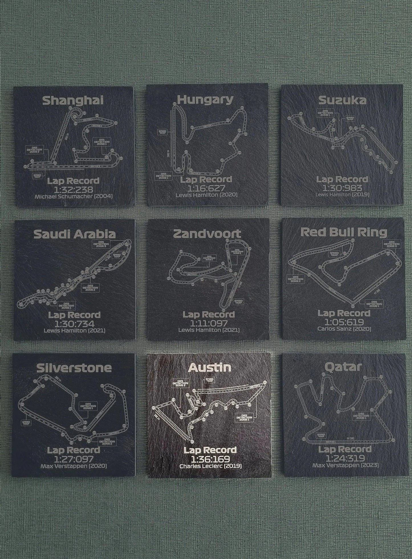 Set of nine dark grey slate coasters, each displaying a Formula 1 circuit map with its lap record. Ideal F1 fan gift.