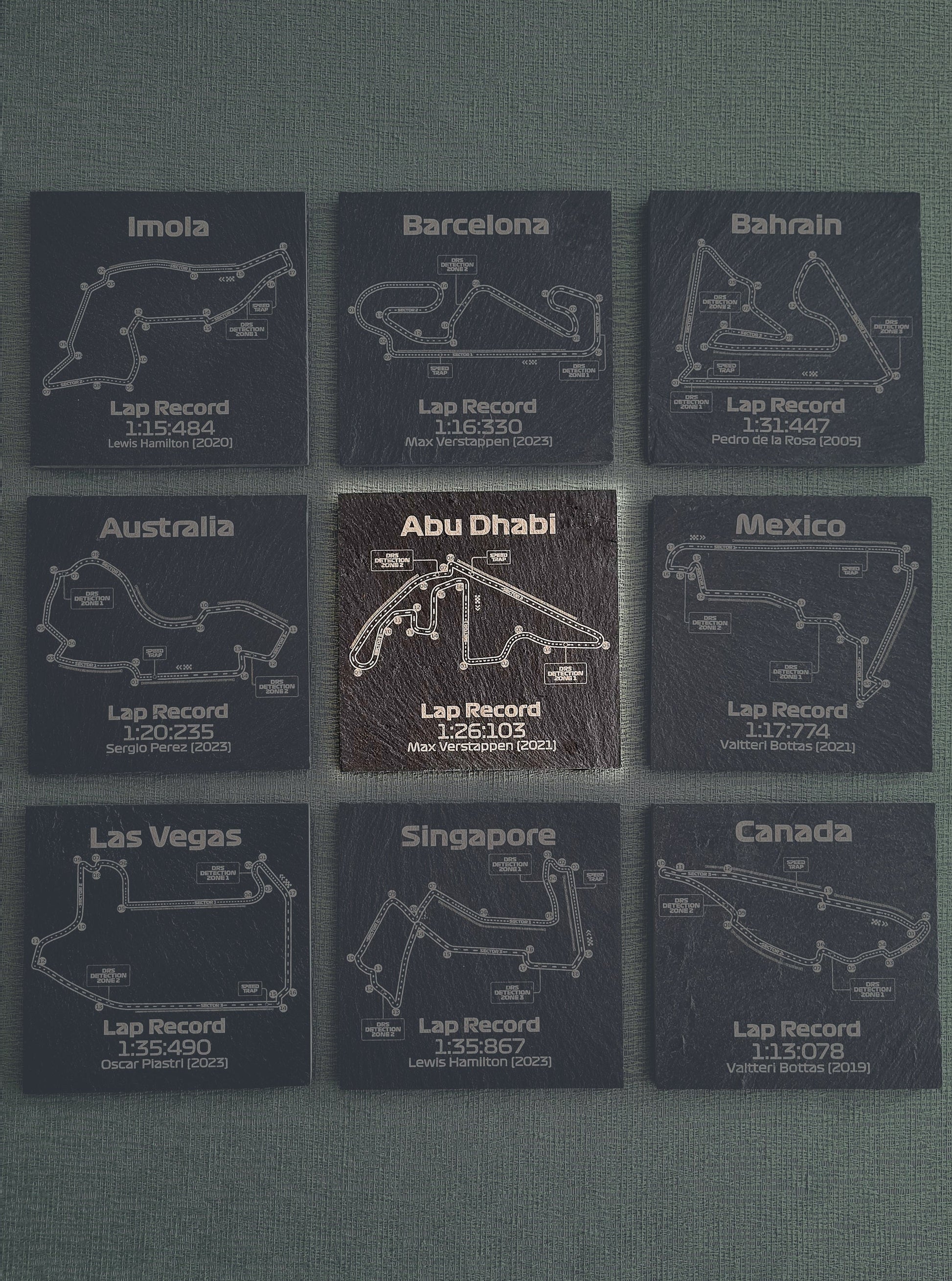 Set of nine dark glass coasters, each featuring different Formula 1 track outlines such as Abu Dhabi, Barcelona, and Mexico, with recorded fastest lap times and drivers' names like Max Verstappen and Lewis Hamilton.
